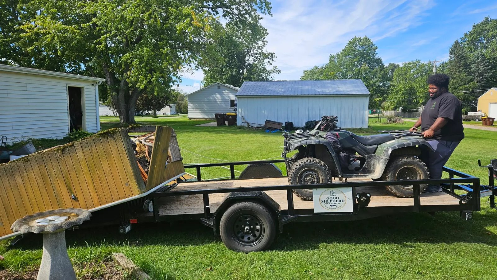 Good Shepherd’s utility trailer being loaded with an ATV and old lumber in a grassy yard